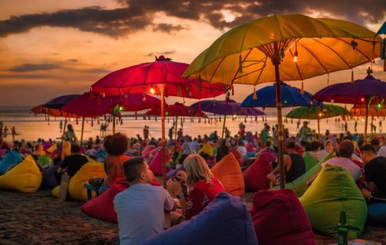 Denpasar, Bali, Indonesia - 17 June 2018: Tourists relaxing and sitting on colorful bean bags, under the umbrellas, and enjoying the sunset at the beach.